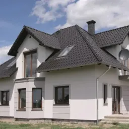 Nowoczesny dom jednorodzinny z ciemną dachówką karpiówką, jasną elewacją i brązowymi oknami, widoczny komin i antena satelitarna.