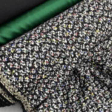 Zbliżenie na wzorzystą tkaninę w odcieniach czerni, bieli i kolorowych kropek, ułożoną obok gładkich, zielonych i czarnych materiałów.