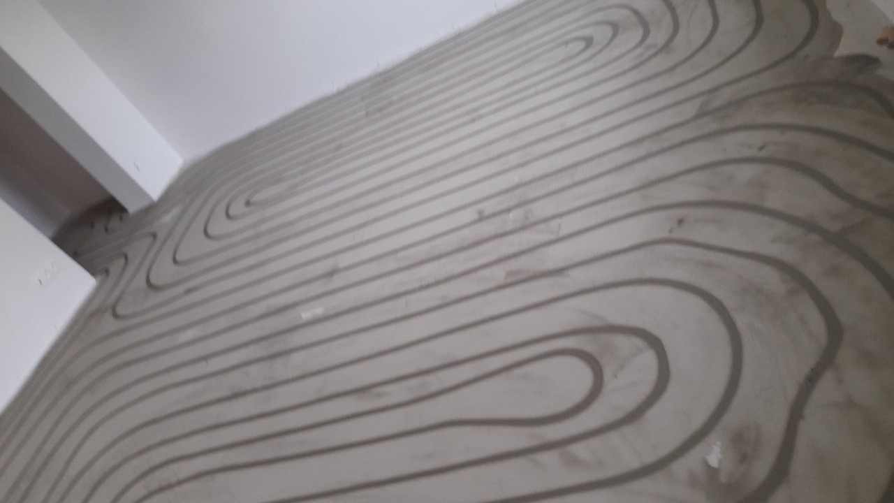 Rury ogrzewania podłogowego ułożone w jastrychu, widoczne zakręty i równoległe linie, surowy stan wykończenia, przygotowanie do wylewki.