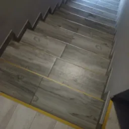 Wykończone schody z szarych płytek imitujących drewno, z żółtymi listwami przypodłogowymi, widok z góry.