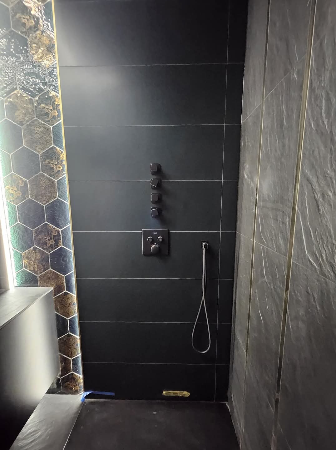 Nowoczesna kabina prysznicowa z czarnymi płytkami i armaturą. Dekoracyjna mozaika heksagonalna. Minimalistyczny design łazienki po remoncie. Detale wykończenia.