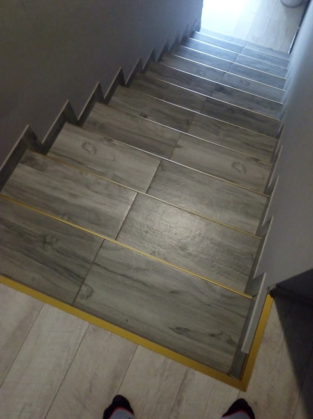 Wykończone schody z szarych płytek imitujących drewno, z żółtymi listwami przypodłogowymi, widok z góry.