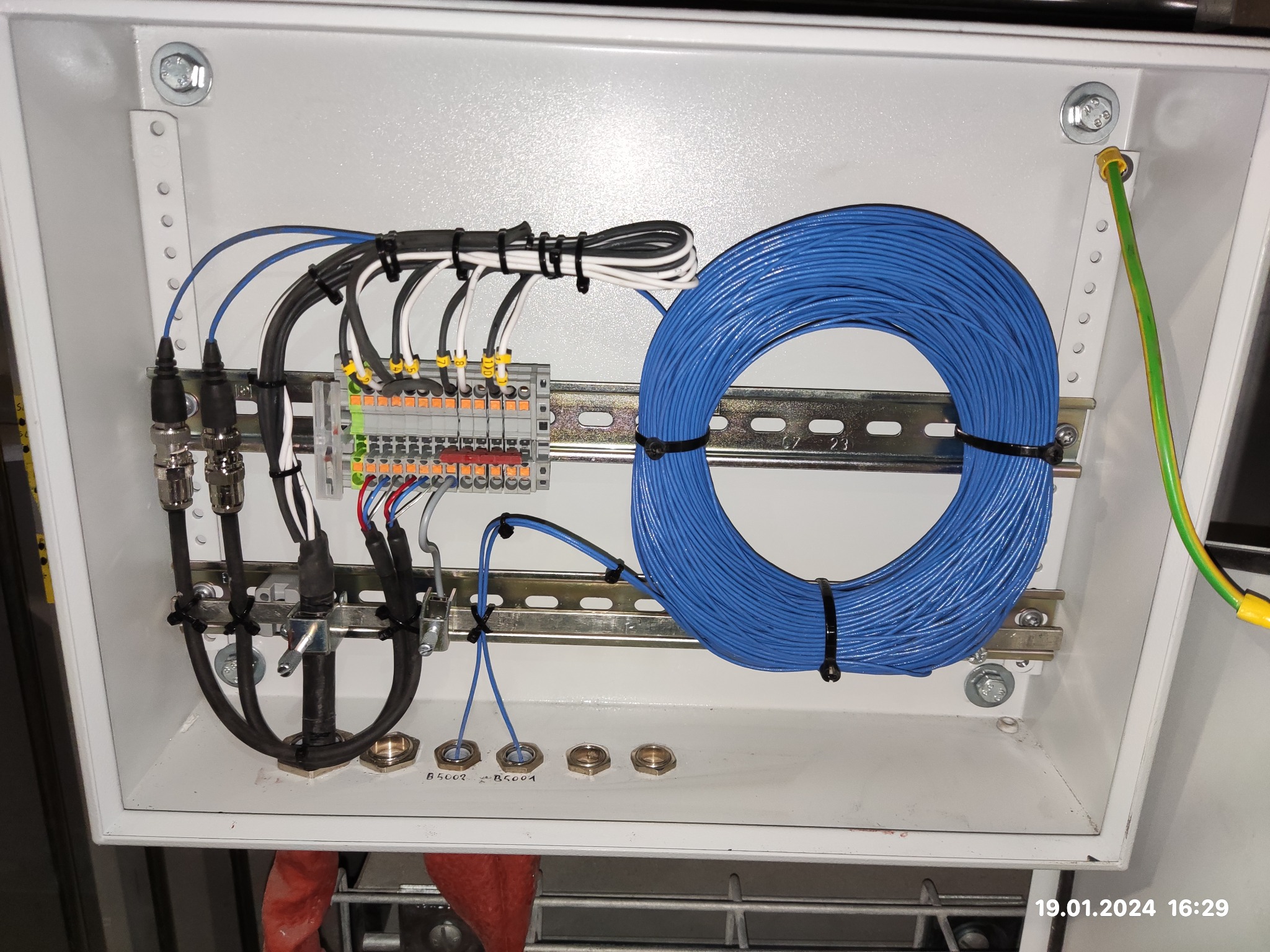 Wnętrze szafy sterowniczej z zamontowanymi elementami: listwa zaciskowa, przewody w peszlach, zwój niebieskiego przewodu zamocowany na szynie DIN, uziemienie.