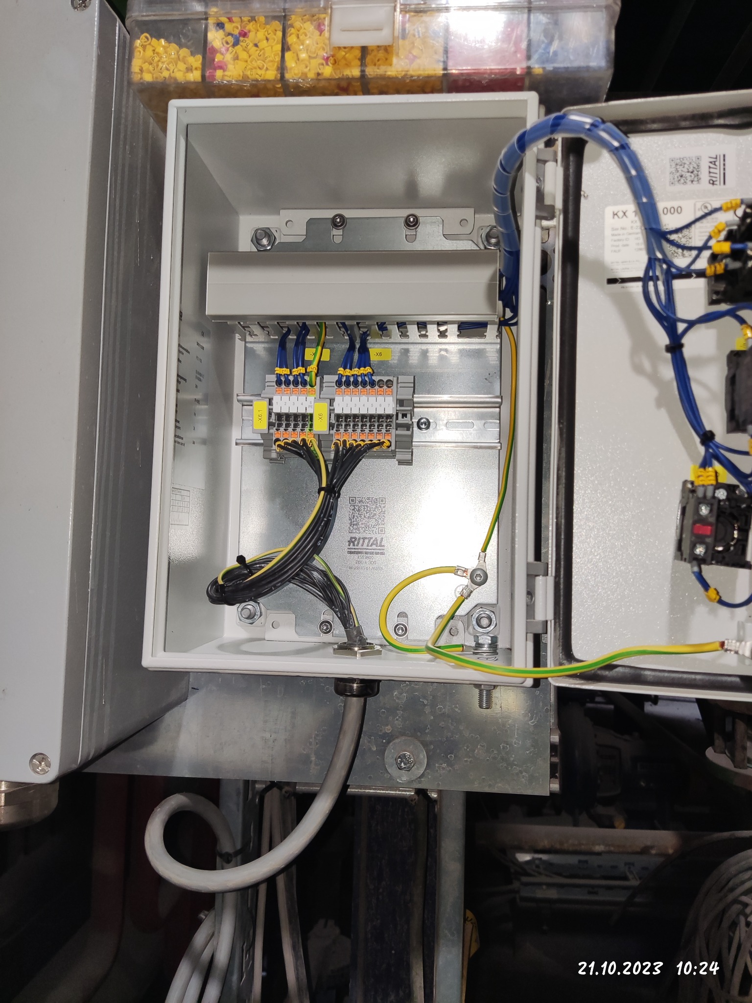 Wnętrze szafy sterowniczej z zamontowanymi listwami zaciskowymi, przewodami w kolorach żółto-zielonym, niebieskim i czarnym, widoczne oznaczenia na listwach i przewodach, obok szafy pojemnik...