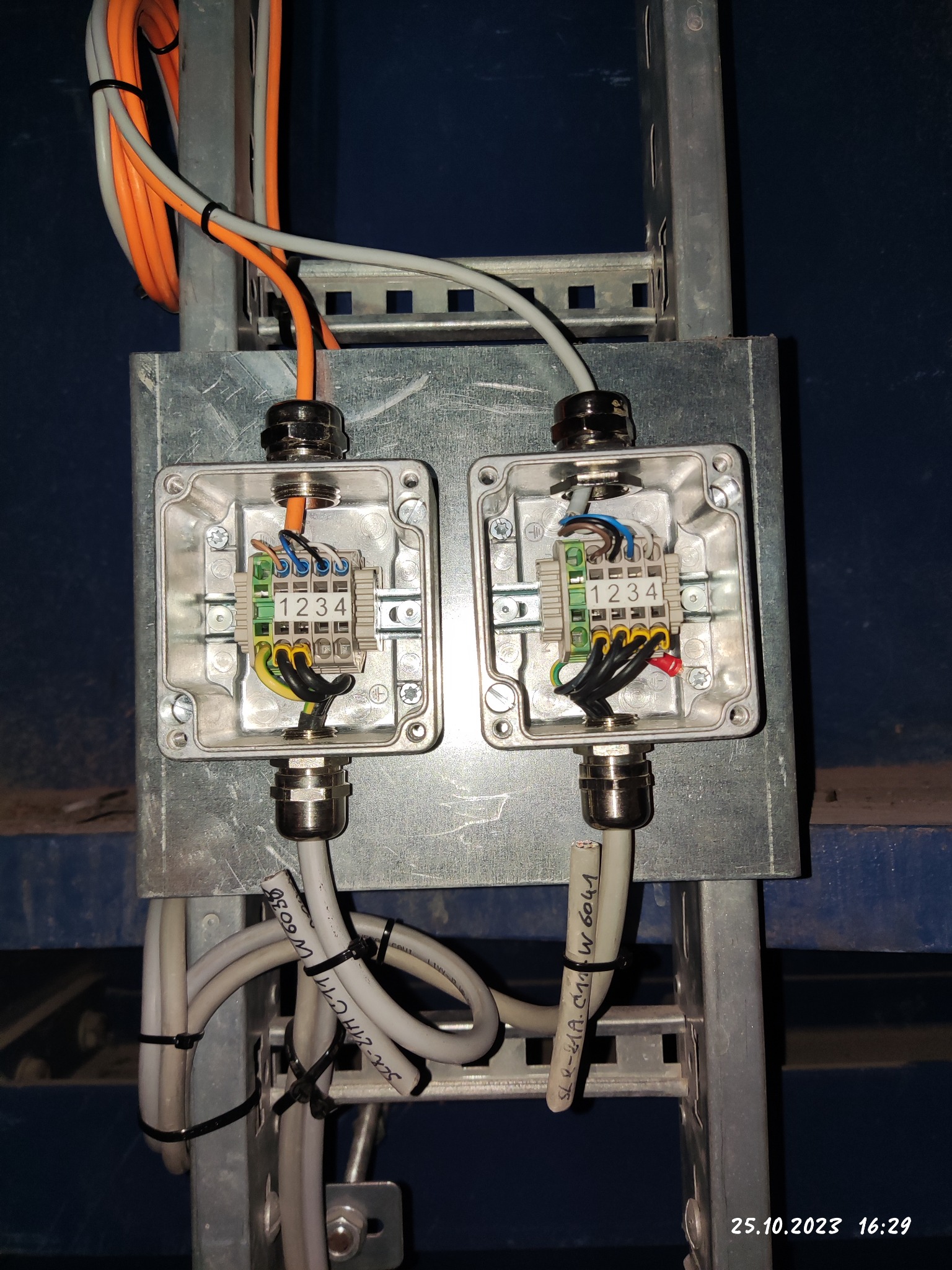 Dwa połączone puszki instalacyjne z widocznymi złączkami i okablowaniem, zamontowane na metalowej drabince kablowej w Kielcach. Na przewodach widoczne opisy.