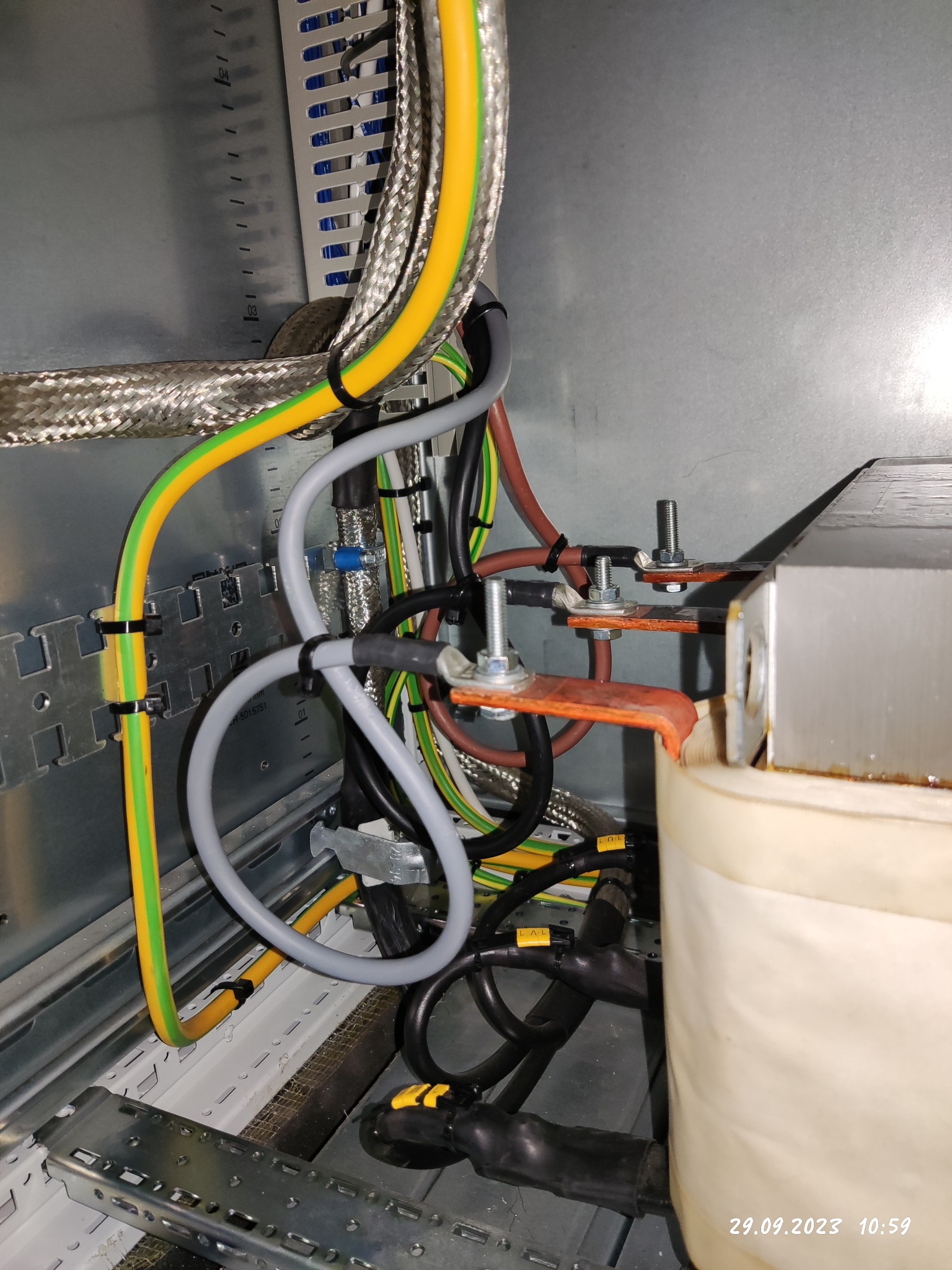 Szczegółowe ujęcie instalacji elektrycznej wewnątrz szafy rozdzielczej z widocznymi przewodami ochronnymi, kablami w oplocie metalowym i elementami mocującymi.