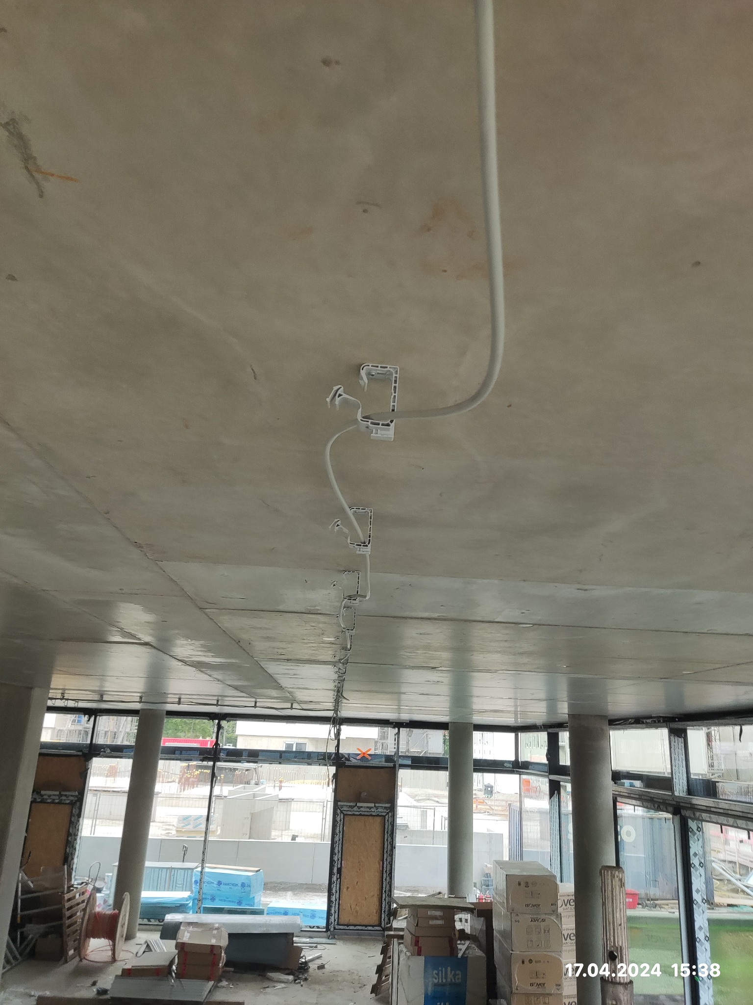 Surowy strop z widocznymi, zamontowanymi puszkami instalacyjnymi i giętką rurą osłonową, prowadzącą instalację elektryczną; widok z dołu w surowym stanie deweloperskim.