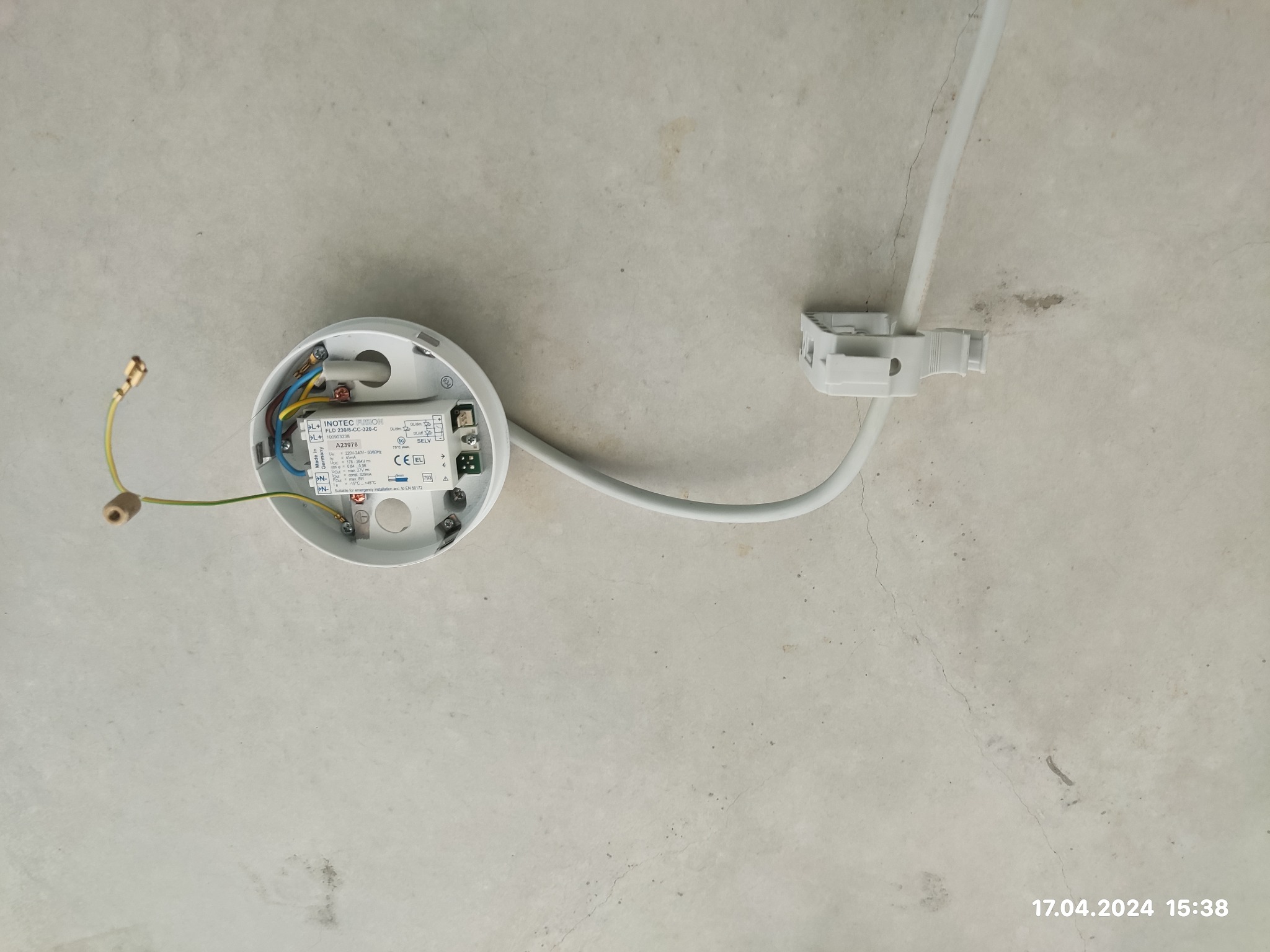 Podłączenie oprawy oświetleniowej do sufitu z widoczną puszką przyłączeniową, przewodami i elementami montażowymi.