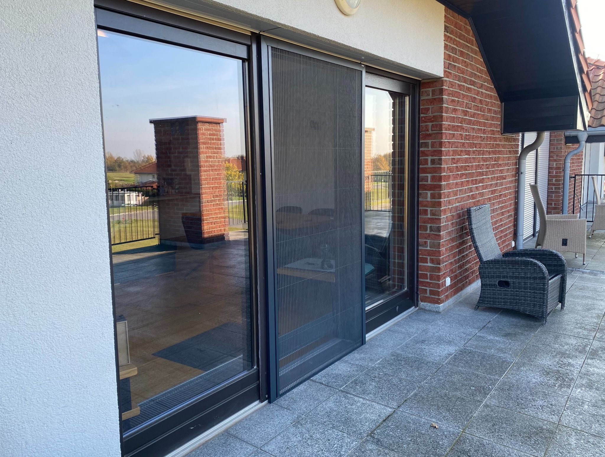 Zewnętrzna moskitiera przesuwna w czarnej ramie, zamontowana na tarasie z widokiem na ogród.