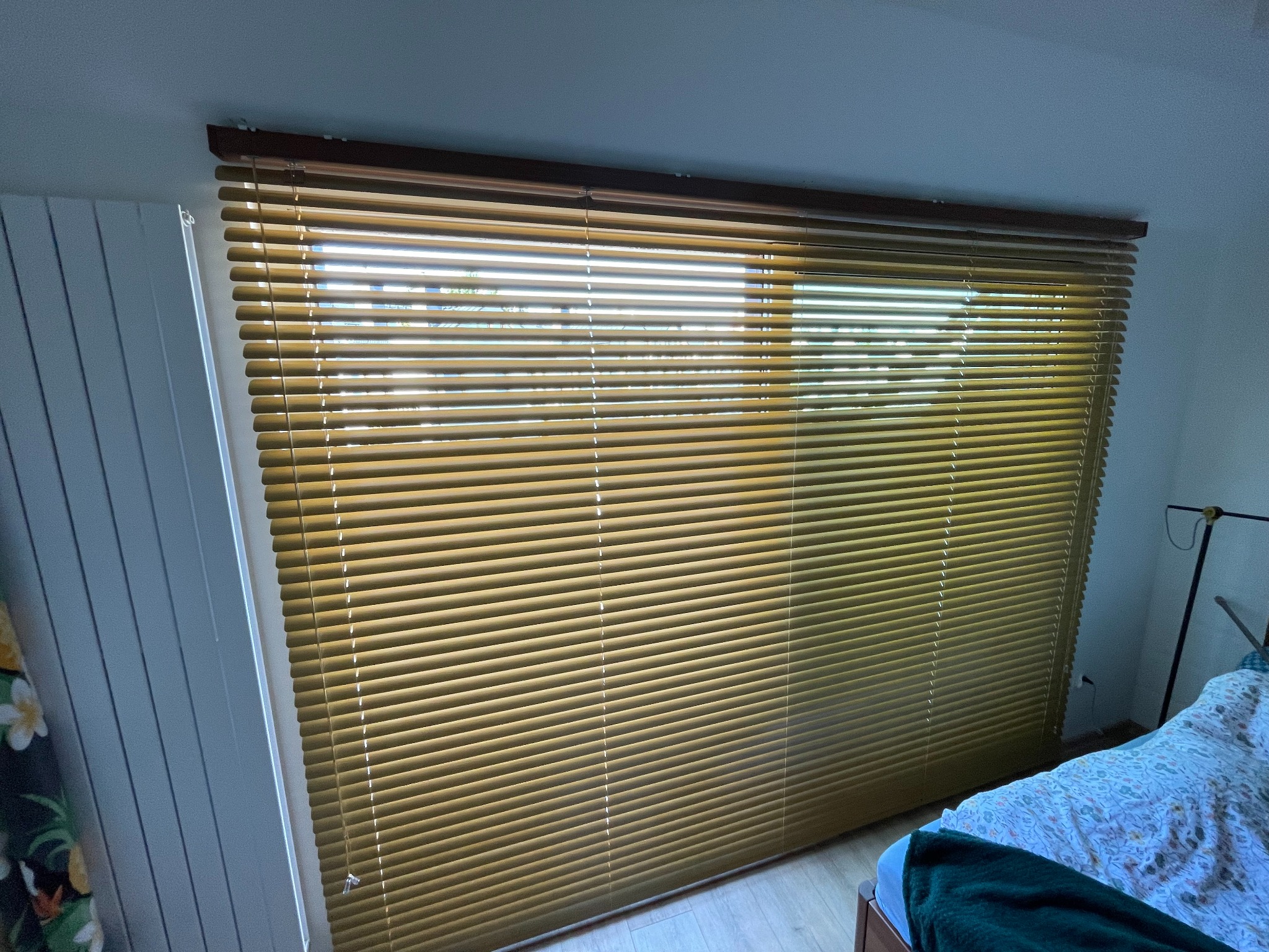 Złote żaluzje poziome zamontowane w oknie, widoczne z wnętrza pokoju, z delikatnym światłem dziennym przesączającym się przez lamele.