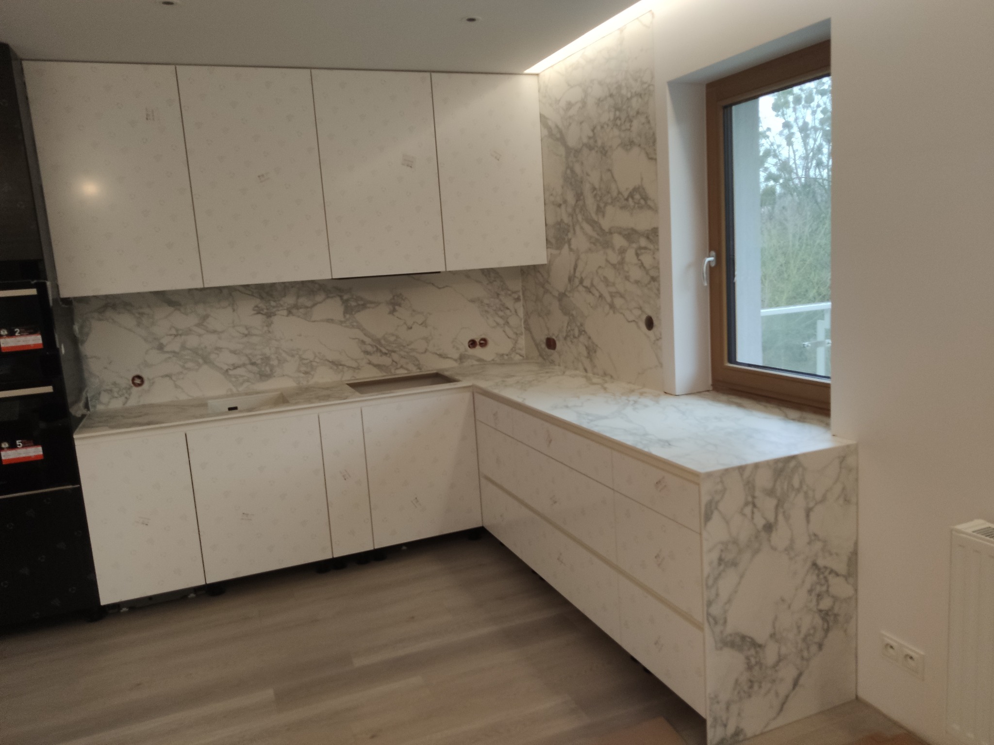 Nowoczesna kuchnia w Poznaniu z białymi szafkami i blatem imitującym marmur, zintegrowanym z parapetem okiennym, widok na jasną podłogę.
