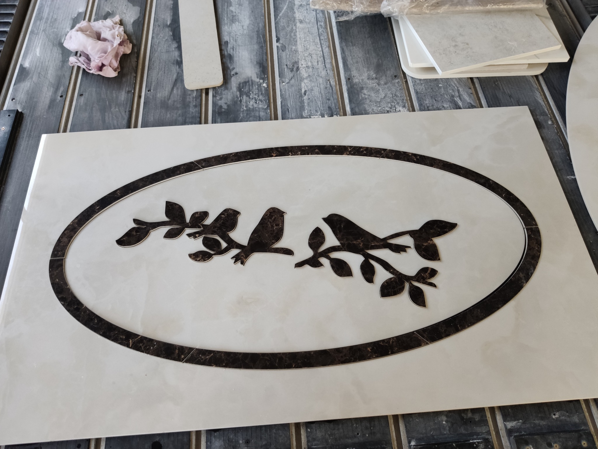 Biały blat z owalnym, ciemnobrązowym obramowaniem i motywem dwóch ptaków siedzących na gałęziach, wykonany z kamienia.