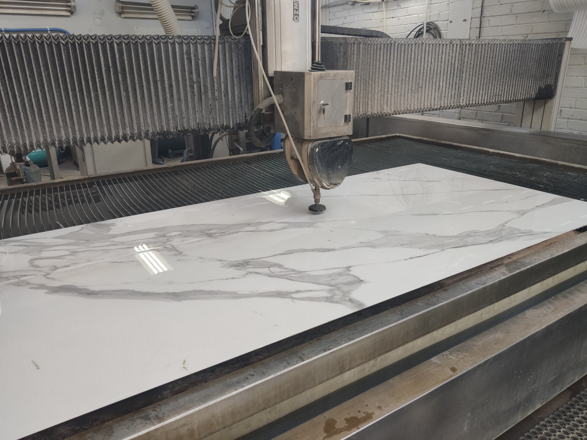 Proces cięcia wodą pod ciśnieniem płyty z białego konglomeratu z szarym marmurowym wzorem na specjalistycznej maszynie.