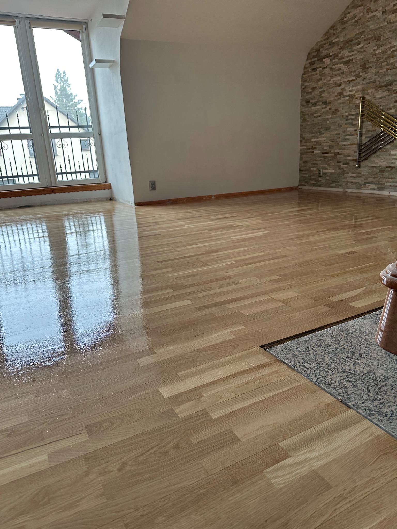 Błyszcząca, świeżo polakierowana podłoga z parkietu w pustym pokoju z oknami i dekoracyjną ścianą z kamienia.