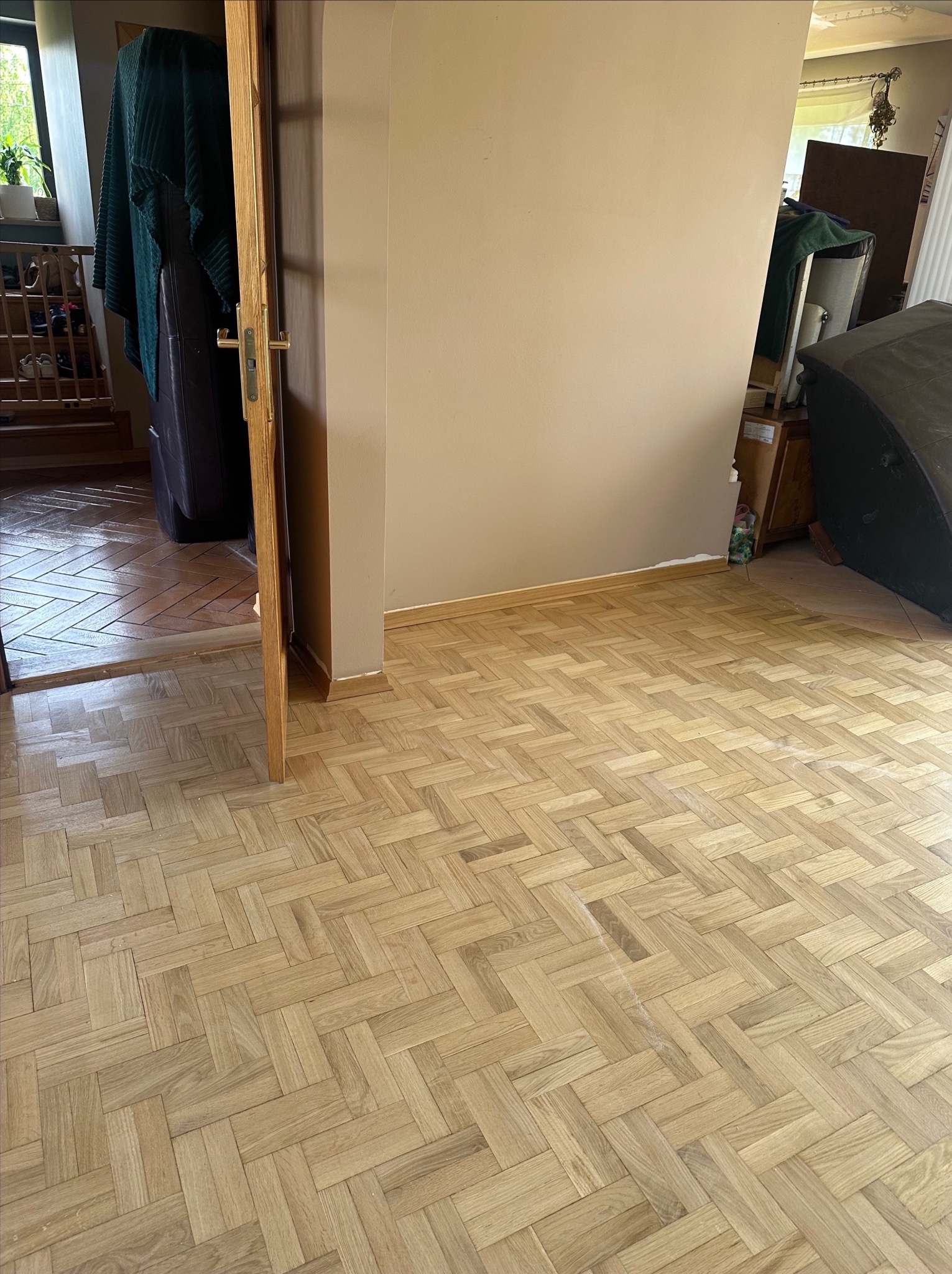 Parkiet ułożony w jodełkę po renowacji, widoczne listwy przypodłogowe. Częściowo otwarte drzwi do kolejnego pomieszczenia z innym rodzajem podłogi.