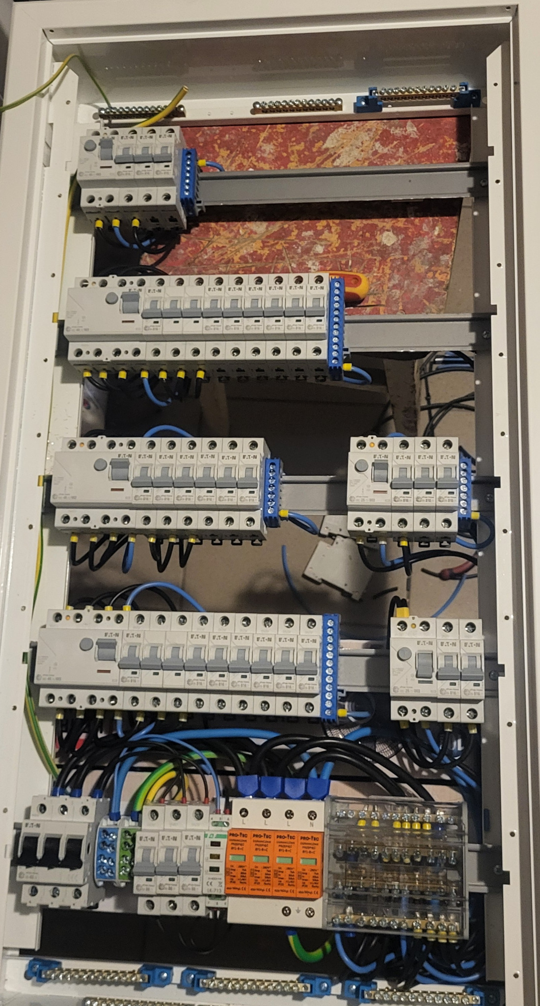 Rozdzielnia elektryczna w białej obudowie, widoczne zabezpieczenia różnicowoprądowe, bezpieczniki, listwy zaciskowe i okablowanie. Zasilanie w trakcie podłączania.