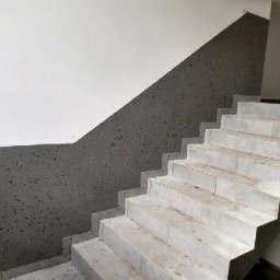 RM Produkcja - Wykończone schody z szarymi ścianami o nieregularnej fakturze. Górna część ścian biała, kontrastująca z ciemniejszą dolną częścią. Widoczne stopnie schodów.