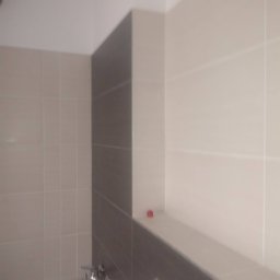 RM Produkcja - Minimalistyczna łazienka: beżowe i szare płytki, bateria wannowa. Ukończone wykończenie z subtelną półką. Czyste linie i neutralna kolorystyka.