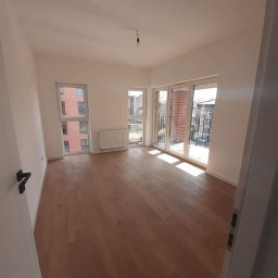 RM Produkcja - Jasne panele podłogowe, świeżo pomalowane białe ściany, okno i drzwi balkonowe w pustym pokoju z grzejnikiem. Widok na miasto z balkonu.