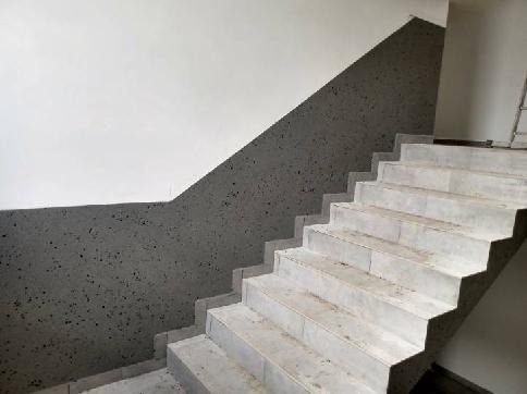 Wykończone schody z szarymi ścianami o nieregularnej fakturze. Górna część ścian biała, kontrastująca z ciemniejszą dolną częścią. Widoczne stopnie schodów.