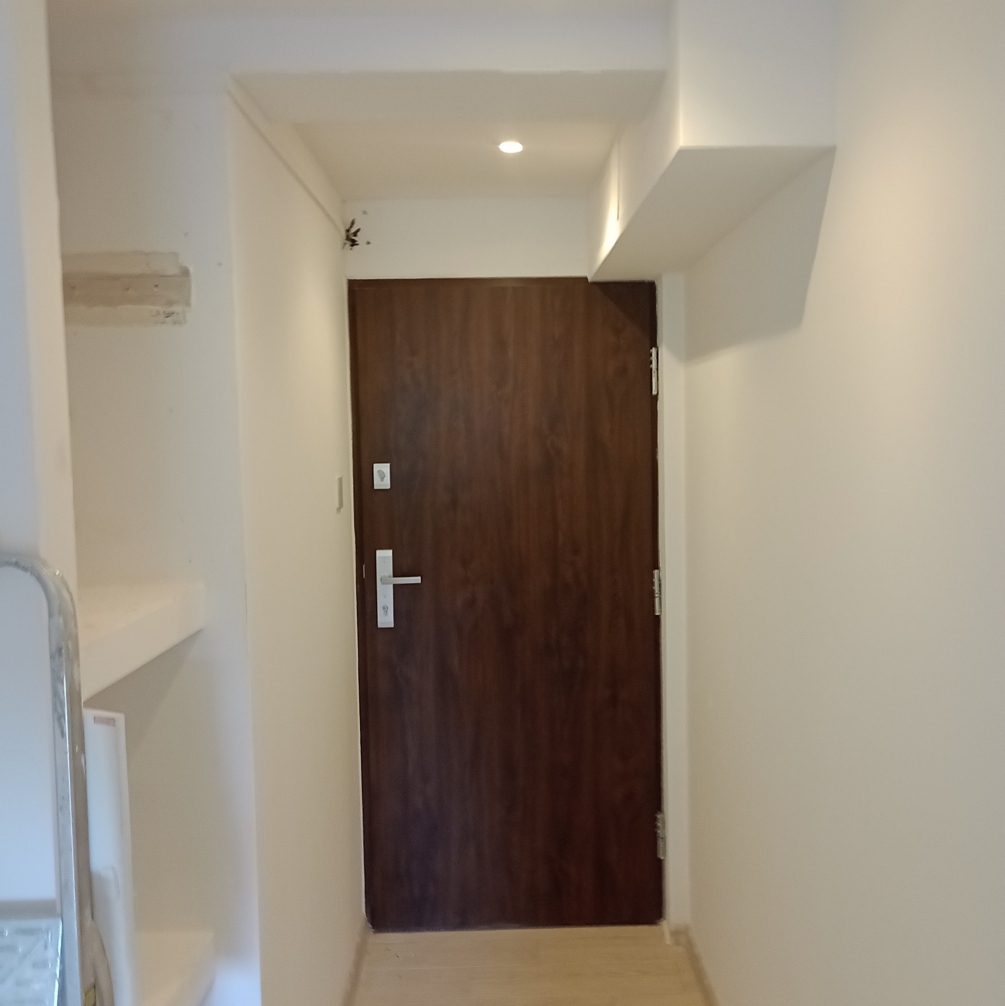 Korytarz po remoncie: świeżo pomalowane, białe ściany z brązowymi drzwiami wejściowymi. Widoczne ślady po instalacji na ścianie.