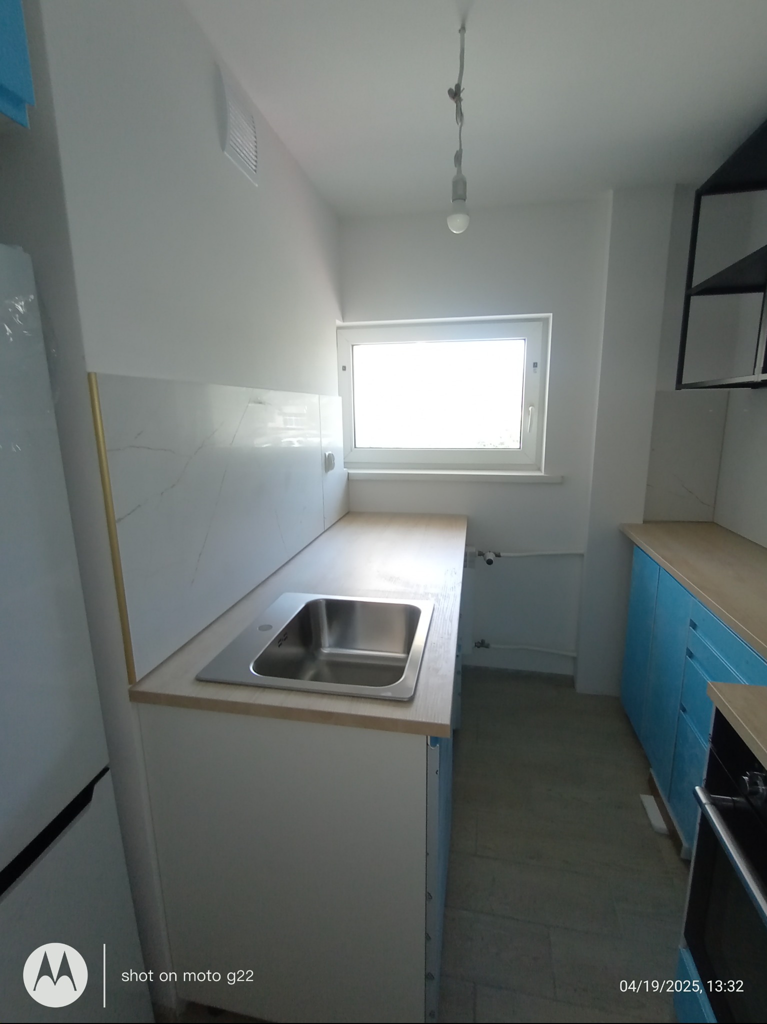 Jasna kuchnia z niebieskimi szafkami, blatem imitującym drewno i marmurowymi panelami ściennymi z subtelnymi złotymi akcentami.