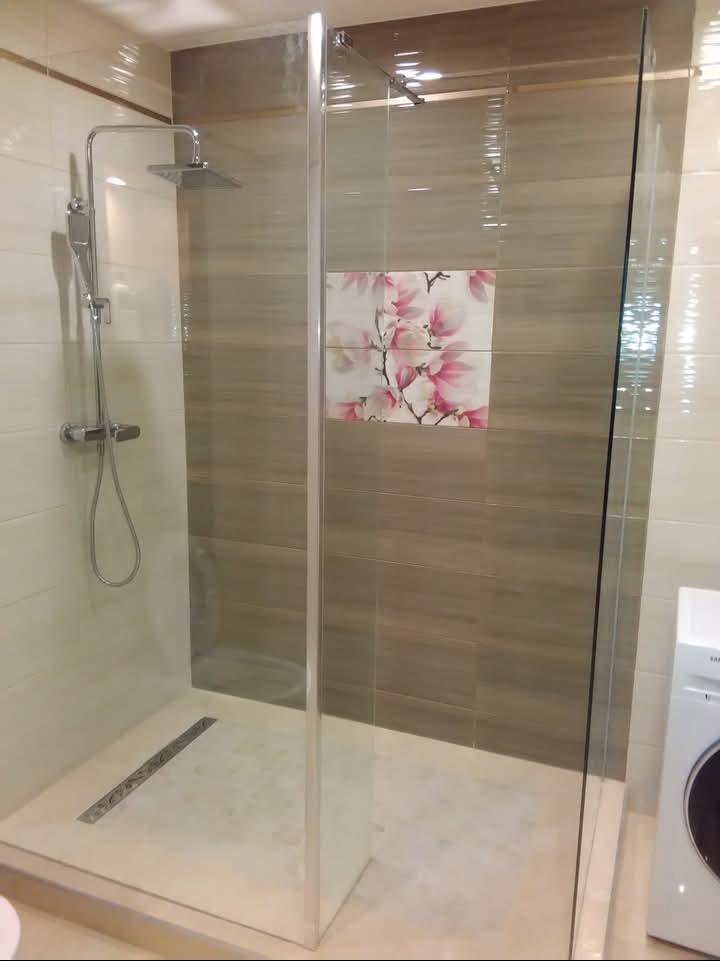 Nowoczesna kabina prysznicowa z deszczownicą i odpływem liniowym, wykończona płytkami w odcieniach beżu i brązu, z dekoracyjnym motywem kwiatowym na ścianie.