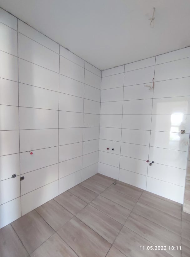 Wykończona łazienka w Katowicach: białe, prostokątne płytki ścienne i podłogowe imitujące drewno. Widoczne przyłącza wod-kan.