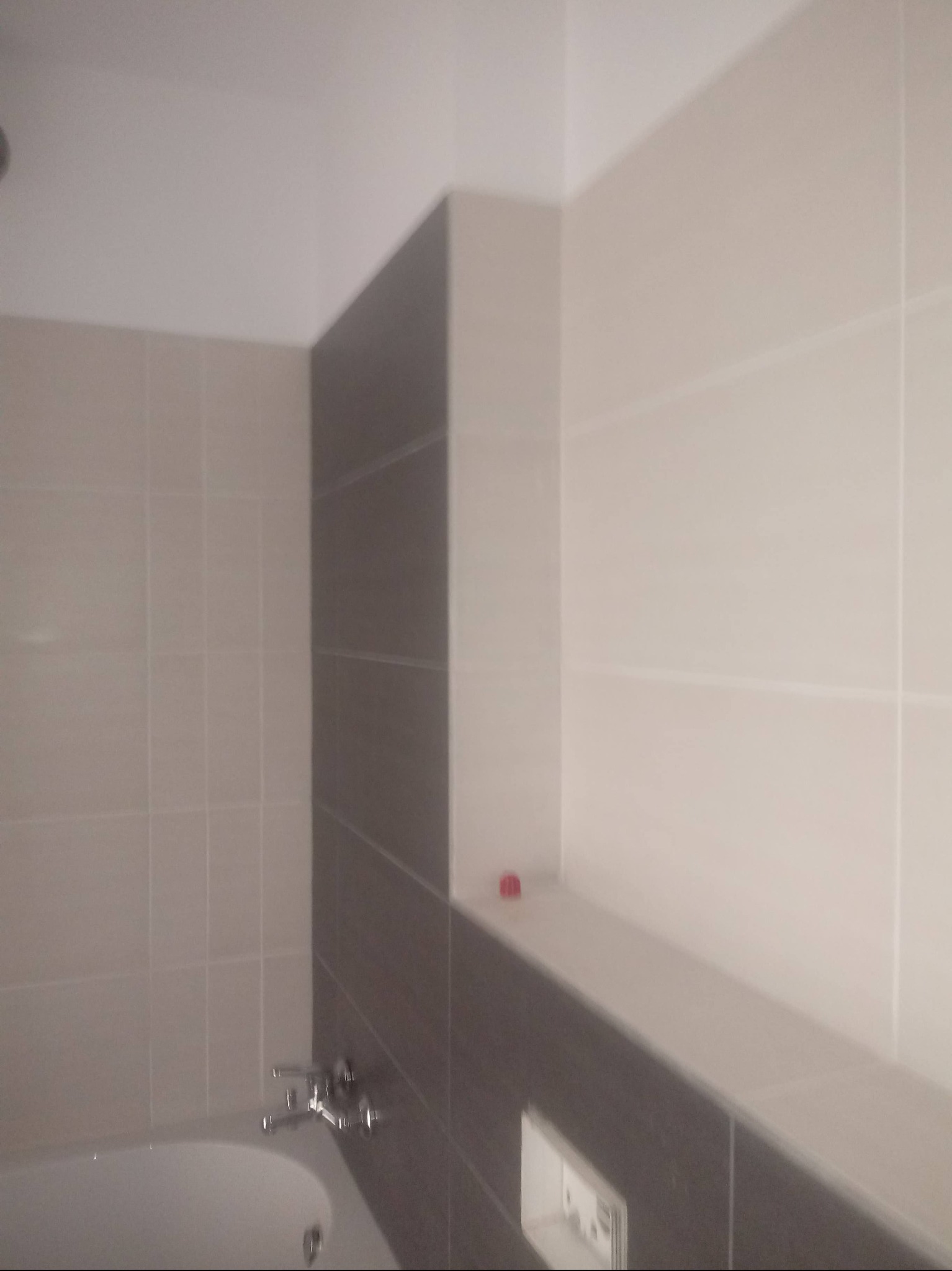 Minimalistyczna łazienka: beżowe i szare płytki, bateria wannowa. Ukończone wykończenie z subtelną półką. Czyste linie i neutralna kolorystyka.