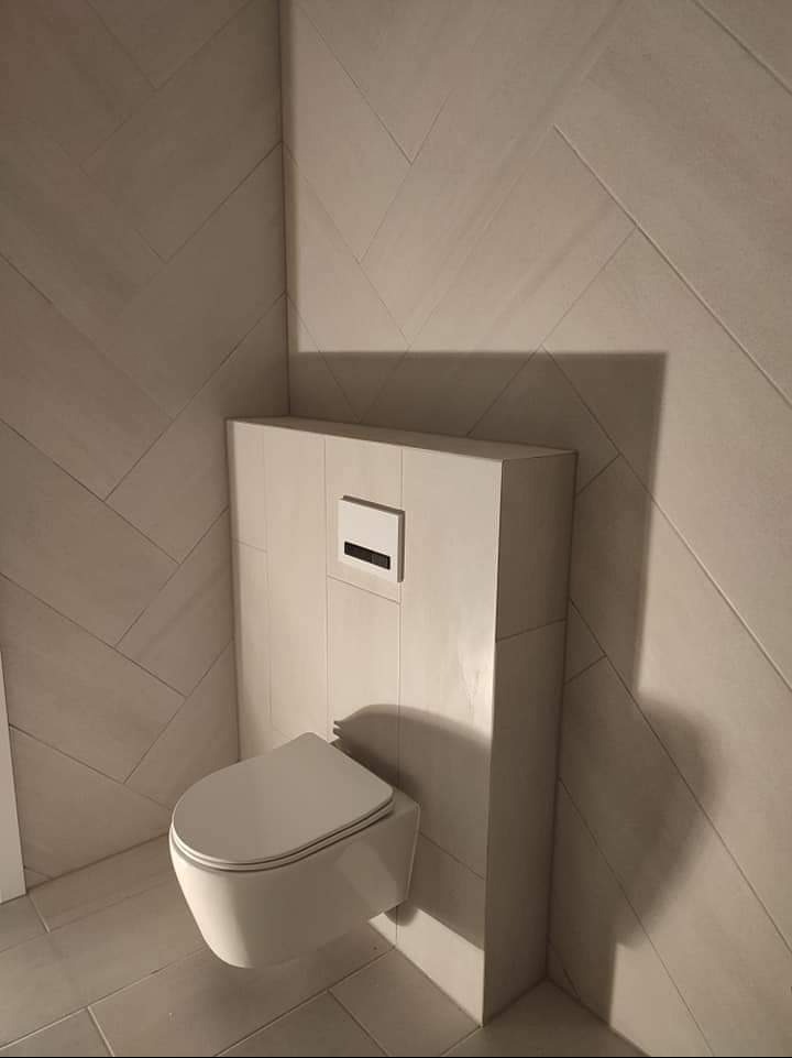 Nowoczesna łazienka z wiszącą toaletą i płytkami ułożonymi w jodełkę. Minimalistyczny design, jasne barwy i precyzyjne wykończenie.