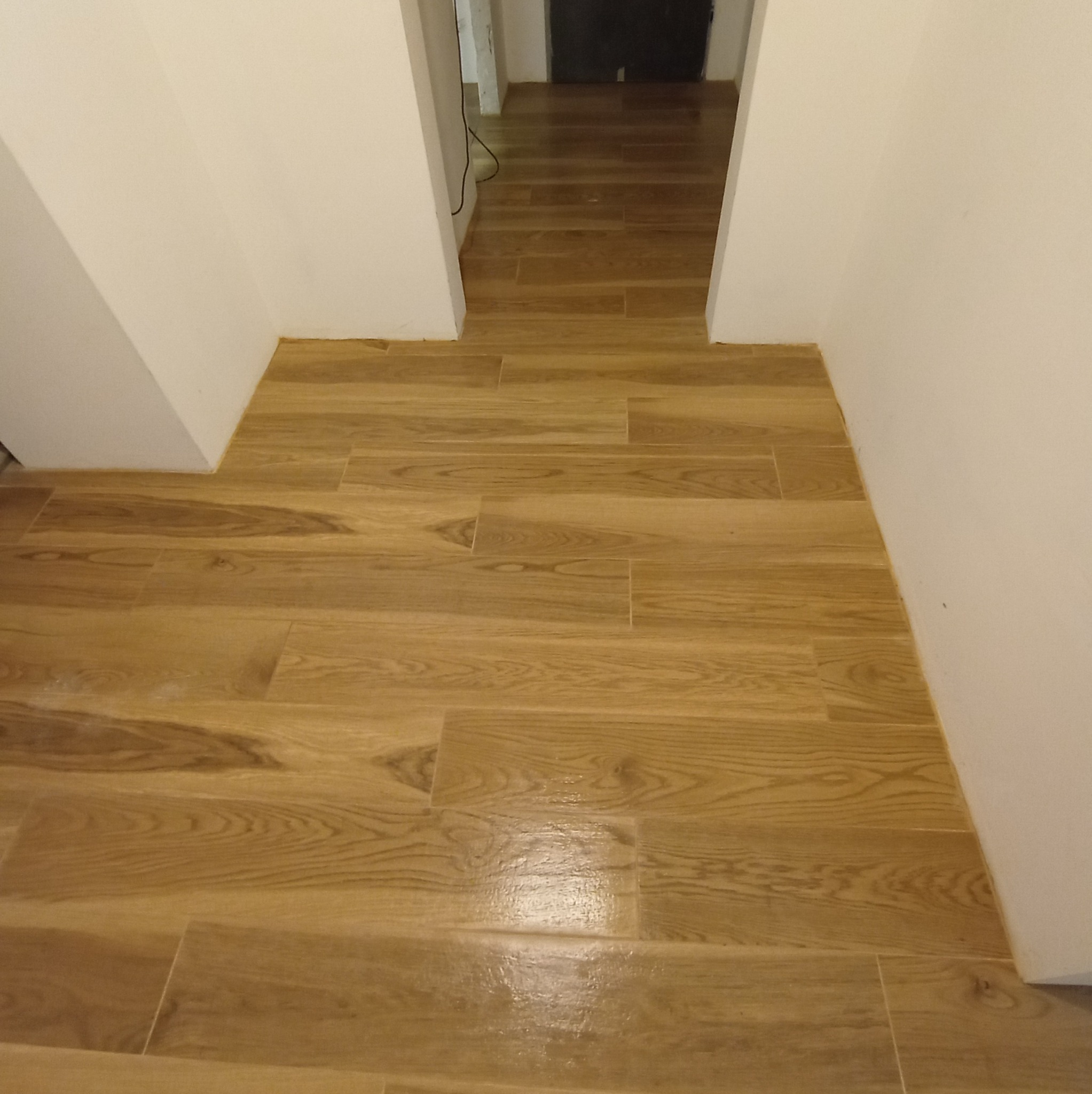 Ułożone panele podłogowe imitujące drewno w korytarzu, widok z góry. Jasne ściany. Widoczne łączenia paneli.