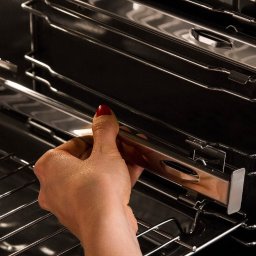 Stanisław Rogala - Wnętrze piekarnika z wysuwanymi prowadnicami teleskopowymi, dłoń z czerwonym paznokciem umieszcza prowadnicę na odpowiednim poziomie.