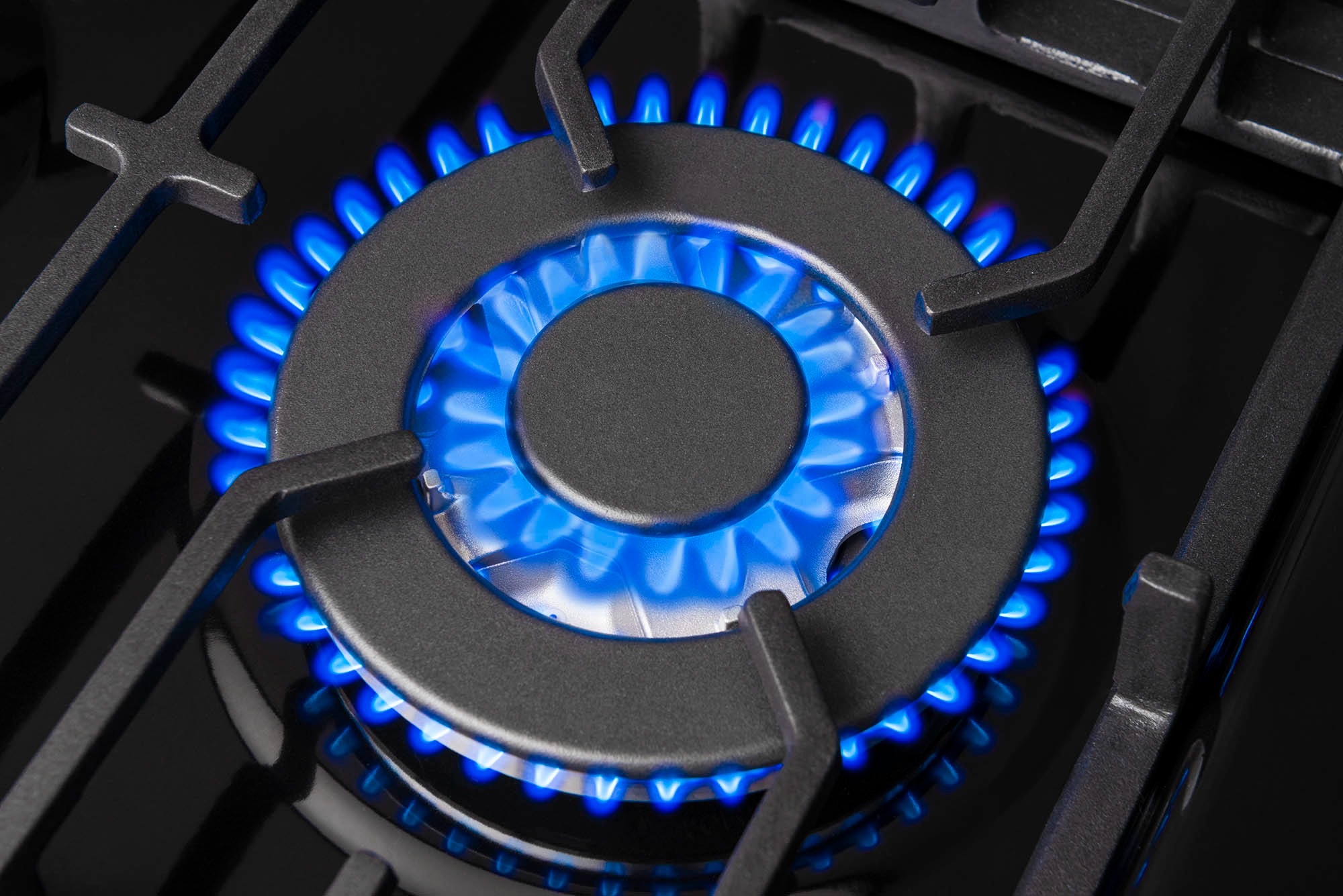 Palnik gazowy kuchenki, płomienie w odcieniach intensywnego błękitu, czarny, żeliwny ruszt, zbliżenie na detale.