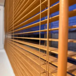 Zamknięte drewniane żaluzje w odcieniach brązu, widok z boku, z niebieskim tłem za oknem.