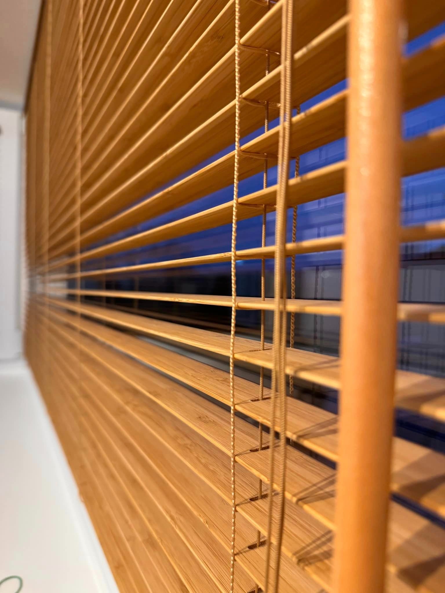 Zamknięte drewniane żaluzje w odcieniach brązu, widok z boku, z niebieskim tłem za oknem.