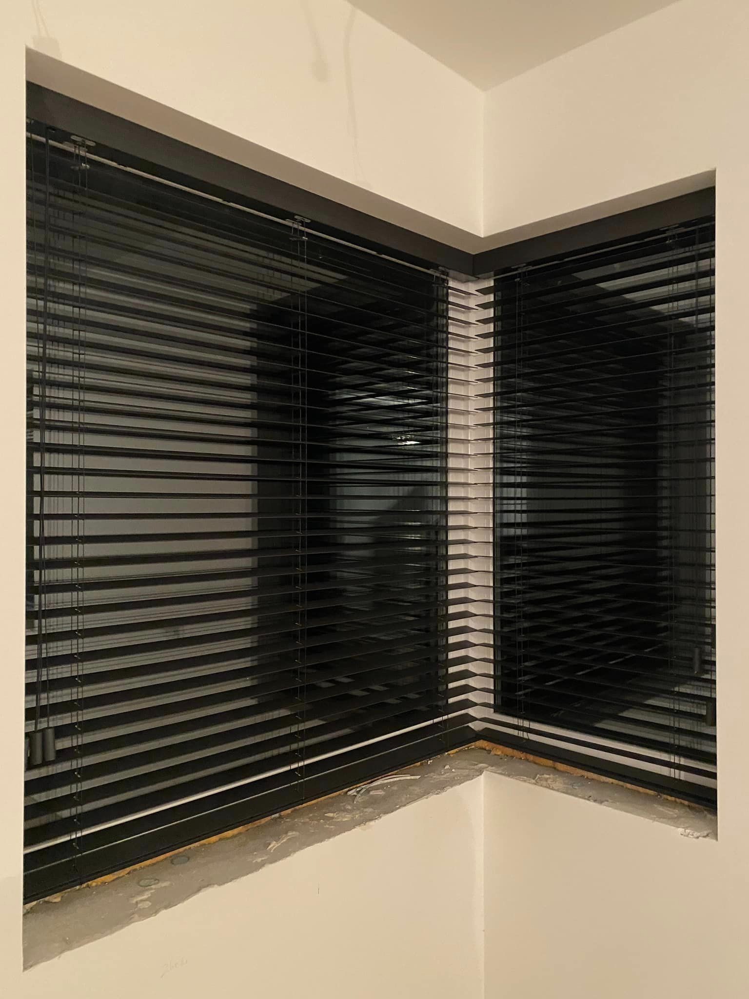 Czarne żaluzje w oknie narożnym, widoczne ślady montażu na parapecie.