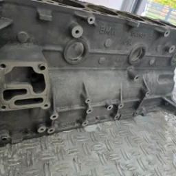 Blok silnika BMW na metalowej powierzchni o strukturze rombów, widoczne otwory i oznaczenia fabryczne.