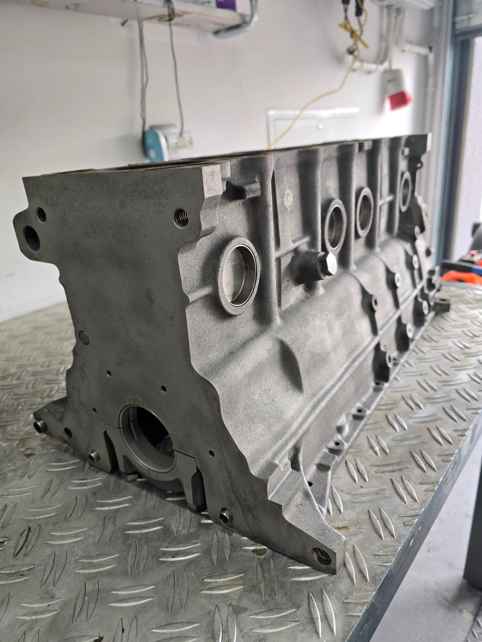 Szary, odnowiony blok silnika spalinowego, leżący na metalowym stole roboczym z blachy ryflowanej.
