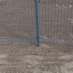 ROMANI GREEN GARDEN ROMAN ROHOVTSOV - Świeżo posiana trawa przy metalowym ogrodzeniu panelowym w Załuskach, widoczne nasiona na ciemnej ziemi.