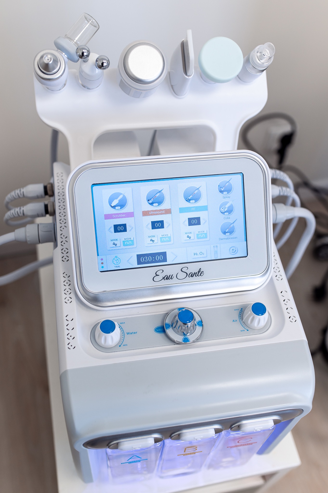 Wielofunkcyjne urządzenie kosmetyczne z wyświetlaczem dotykowym prezentującym opcje zabiegów: Scrubber, Ultrasound, RF, Spray, Cold i Dermabrasion, z widocznymi pojemnikami na płyny i regulacją...