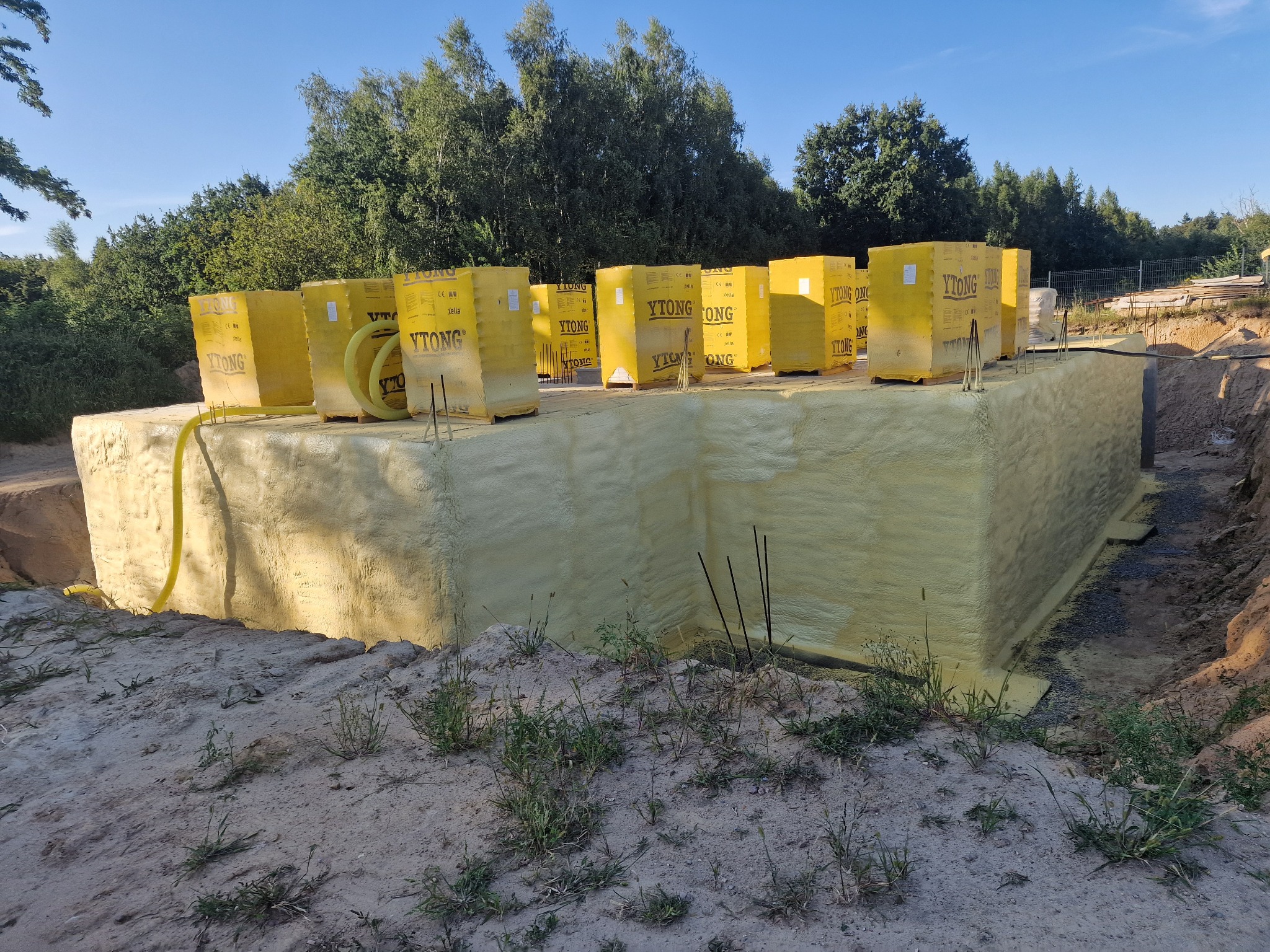 Fundament budynku w Gorzowie Wielkopolskim po izolacji, pokryty warstwą pianki, z paletami bloczków Ytong na górze, widoczne elementy instalacji.