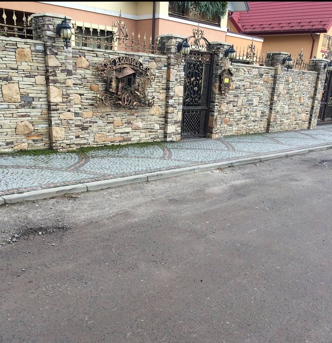 Kamienny mur z kutą bramą i dekoracją w Markach. Solidne ogrodzenie z lampami i brukowanym chodnikiem. Estetyczne wykończenie posesji.