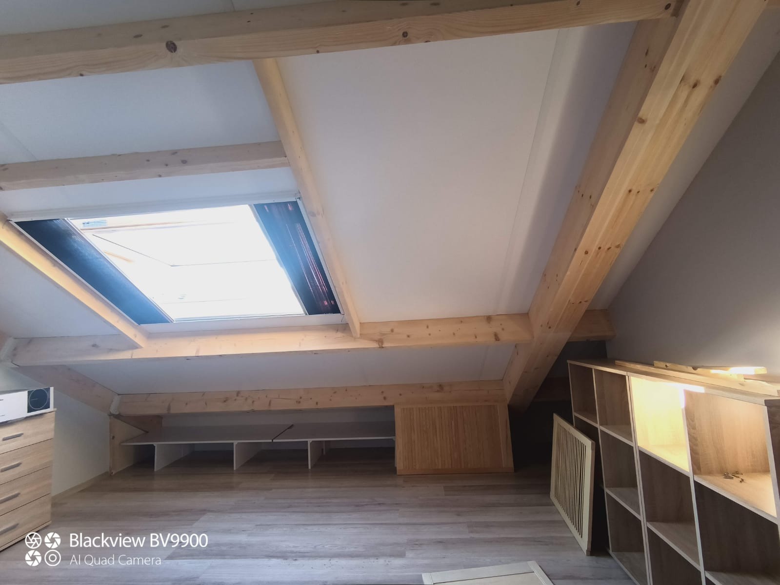 Poddasze z drewnianą konstrukcją nośną, oknem dachowym z roletą i zabudową meblową w trakcie realizacji.