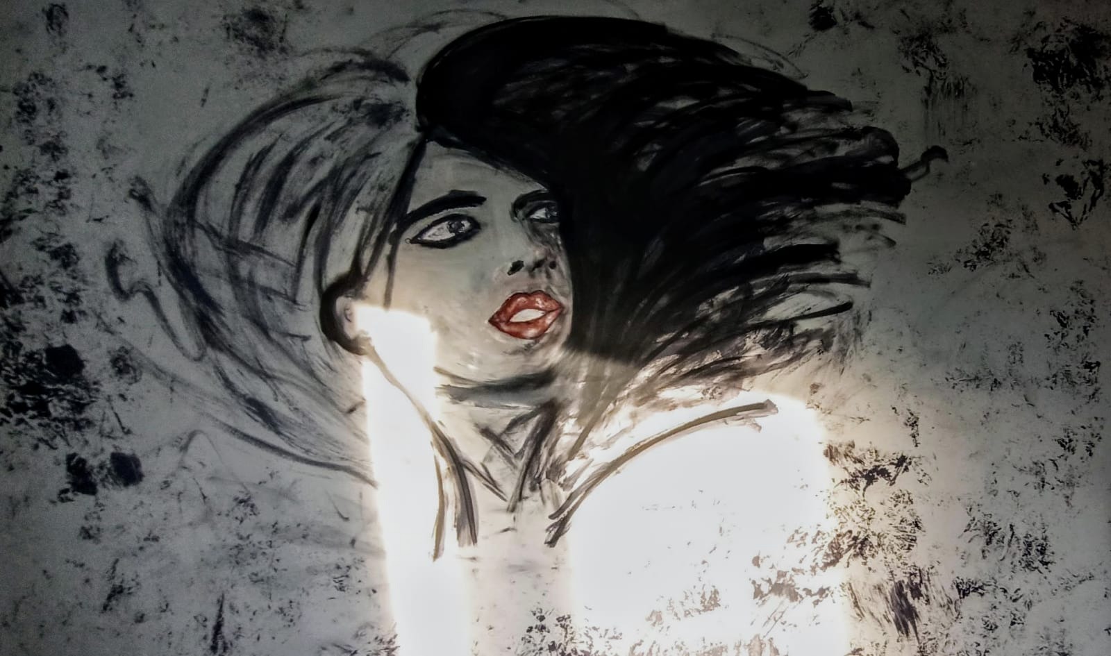 Szkic portretu kobiety z czerwonymi ustami wykonany na ścianie w Grudziądzu, oświetlony od dołu, tworzący artystyczny efekt na wykończonej powierzchni.