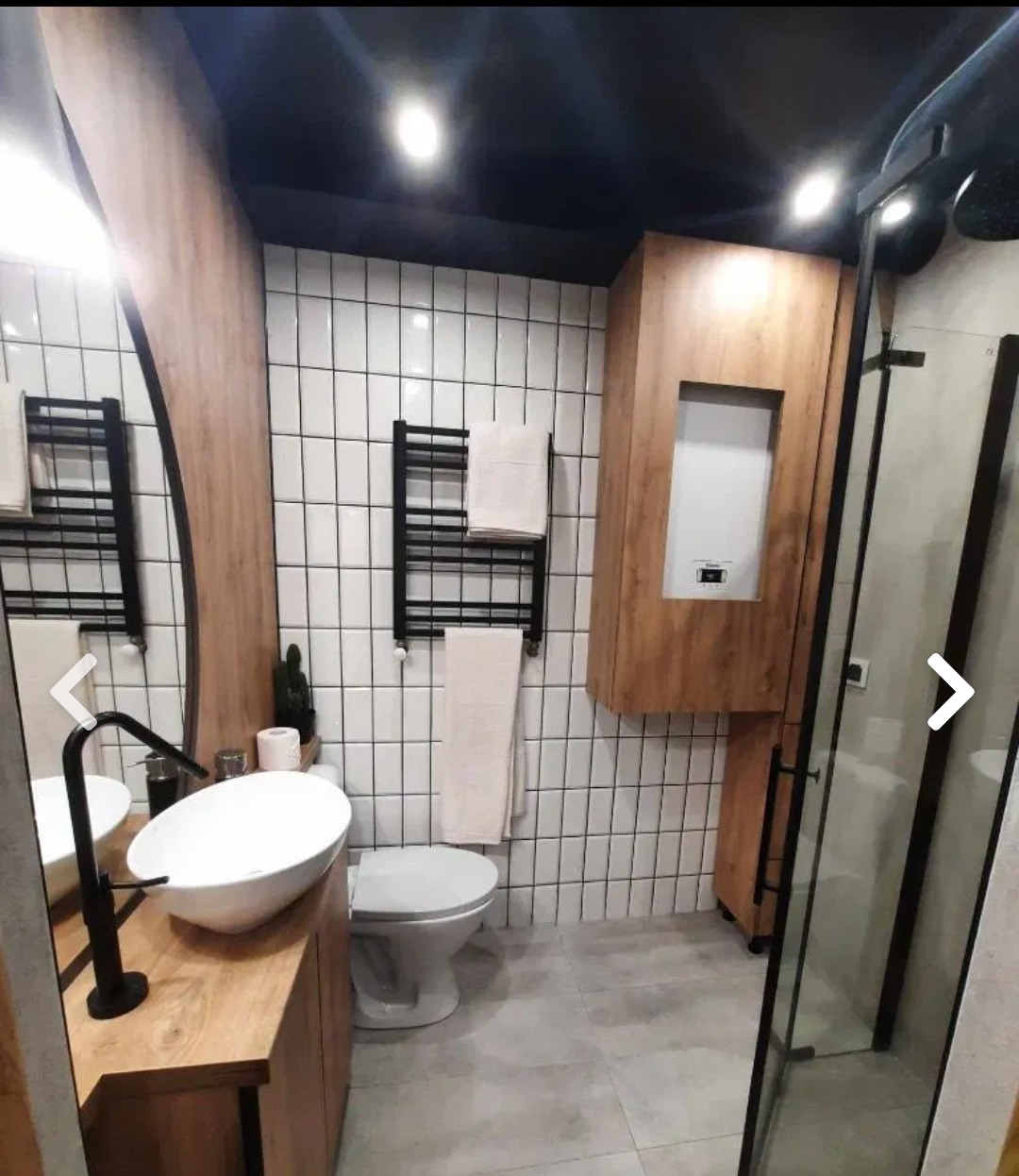 Nowoczesna łazienka w Grudziądzu z owalną umywalką nablatową, czarną armaturą, grzejnikiem drabinkowym i kabiną prysznicową typu walk-in, wykończona białymi, wąskimi kafelkami z ciemną fugą...