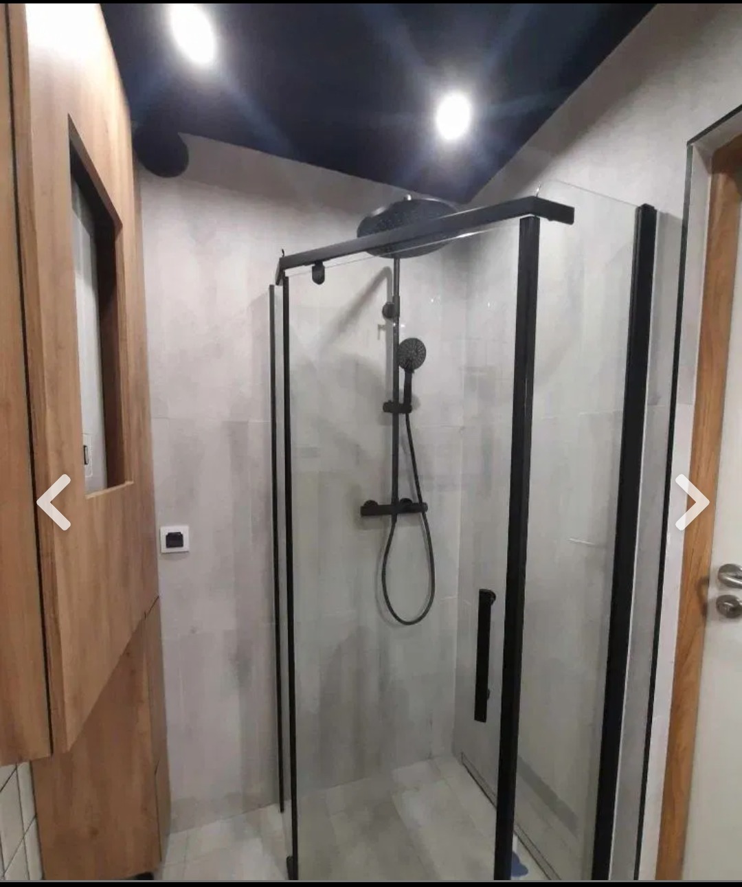 Nowoczesna łazienka z kabiną prysznicową typu walk-in z czarnymi profilami, drewnianą szafką z lustrem i podświetlanym sufitem w kolorze granatowym.