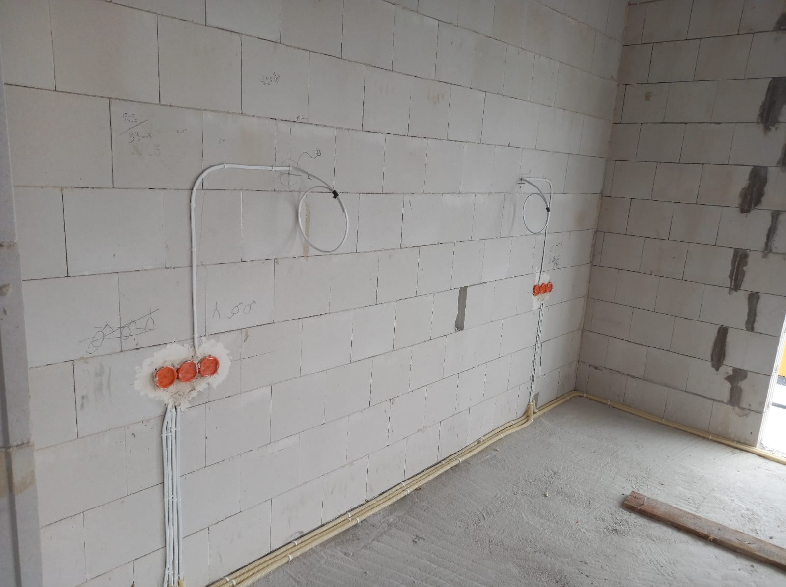 Surowa ściana z betonu komórkowego z widocznymi przewodami elektrycznymi w peszlach oraz puszkami pod gniazdka, etap prac instalacyjnych.