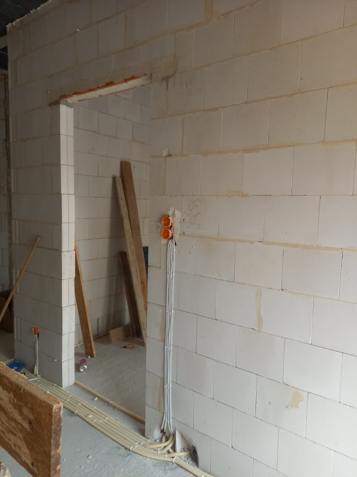 Ściana z betonu komórkowego w trakcie remontu, widoczne puszki elektryczne i przewody w peszlach, surowe drewno w tle.