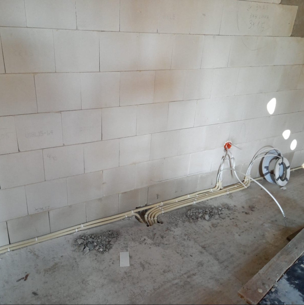 Instalacja przewodów elektrycznych w karbowanych rurach w ścianie z betonu komórkowego, widoczna puszka instalacyjna i zwój kabla.