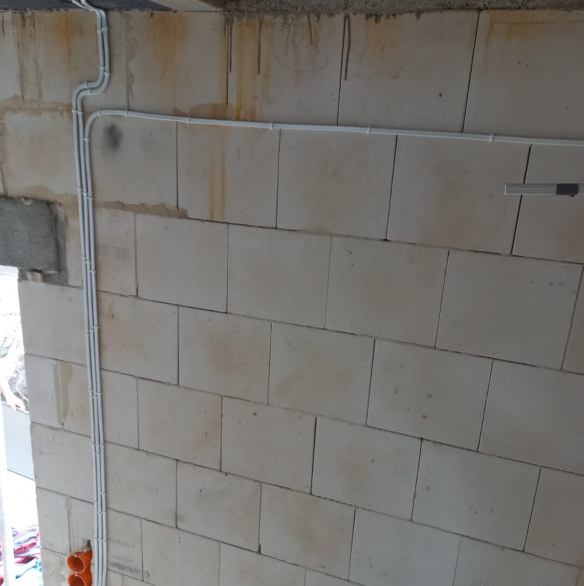 Białe kable elektryczne ułożone wzdłuż ściany z betonu komórkowego w surowym stanie, widoczne puszki instalacyjne.